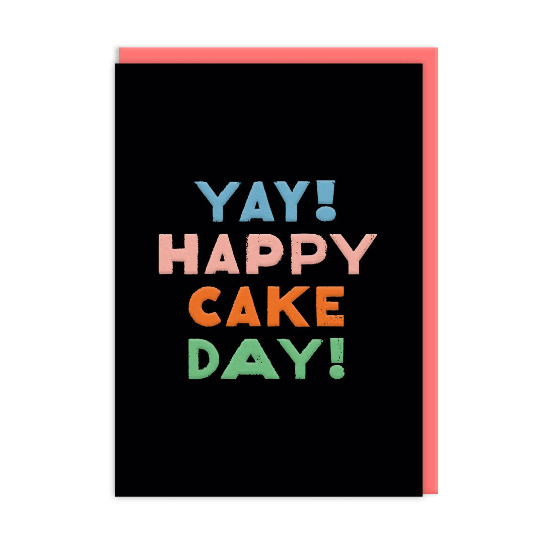 Black birthday card with multi coloured text that reads "Happy Cake Day" and a coral coloured envelope