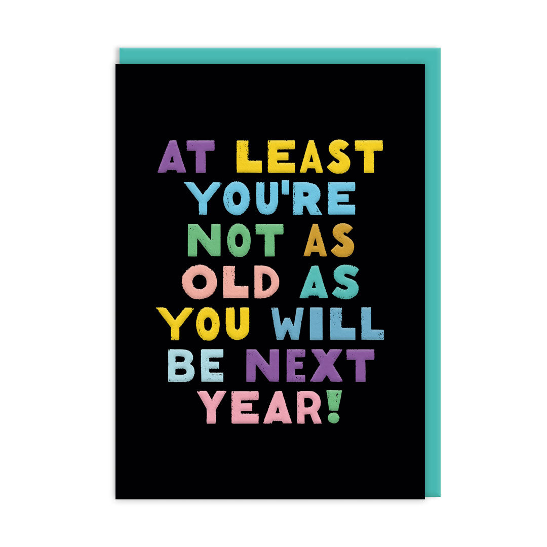 Black birthday card with multi coloured text that reads "At Least You're Not As Old As You Will BE Next Year" and accompanying Aqua coloured envelope