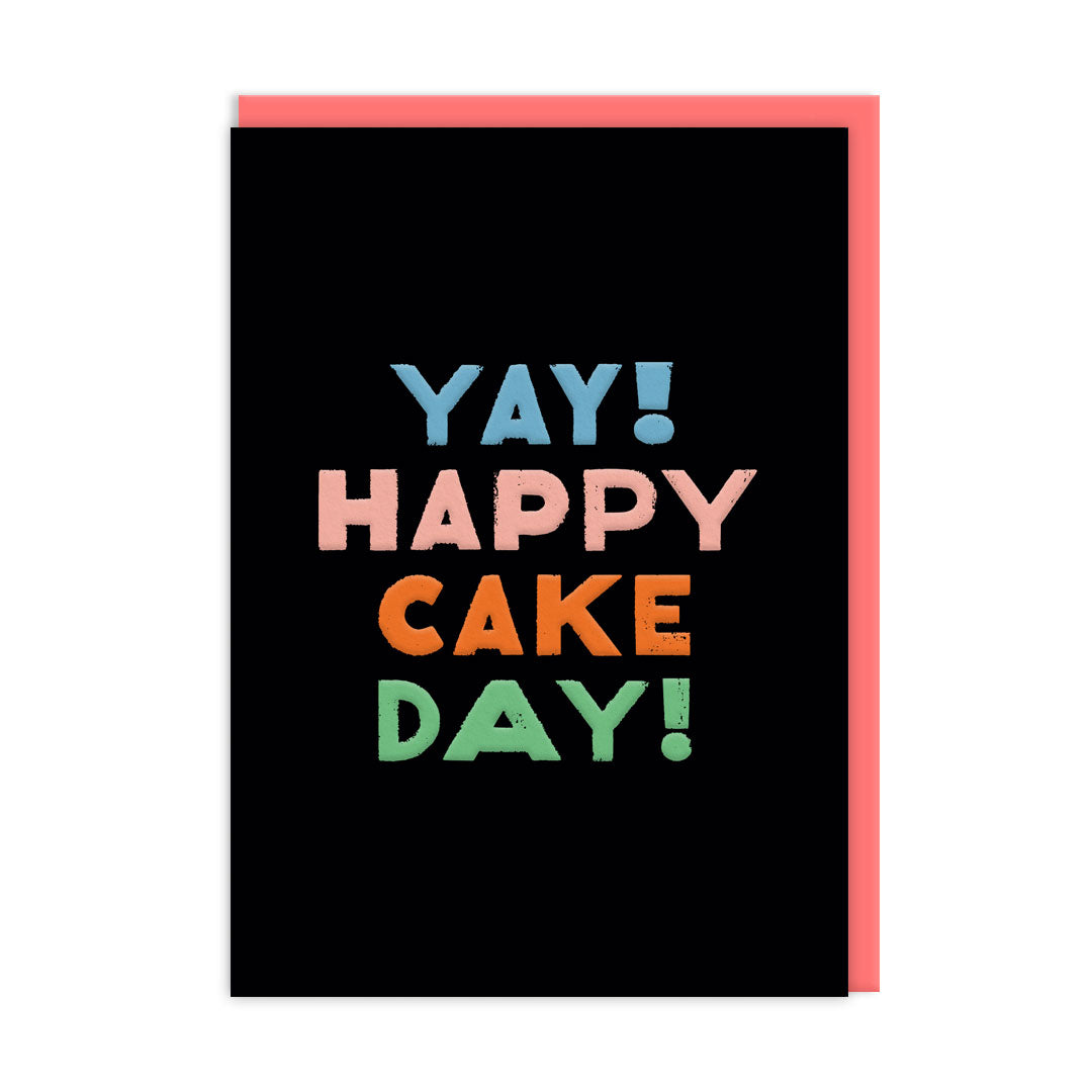 Black birthday card with multi coloured text that reads "Happy Cake Day"  and a coral coloured envelope